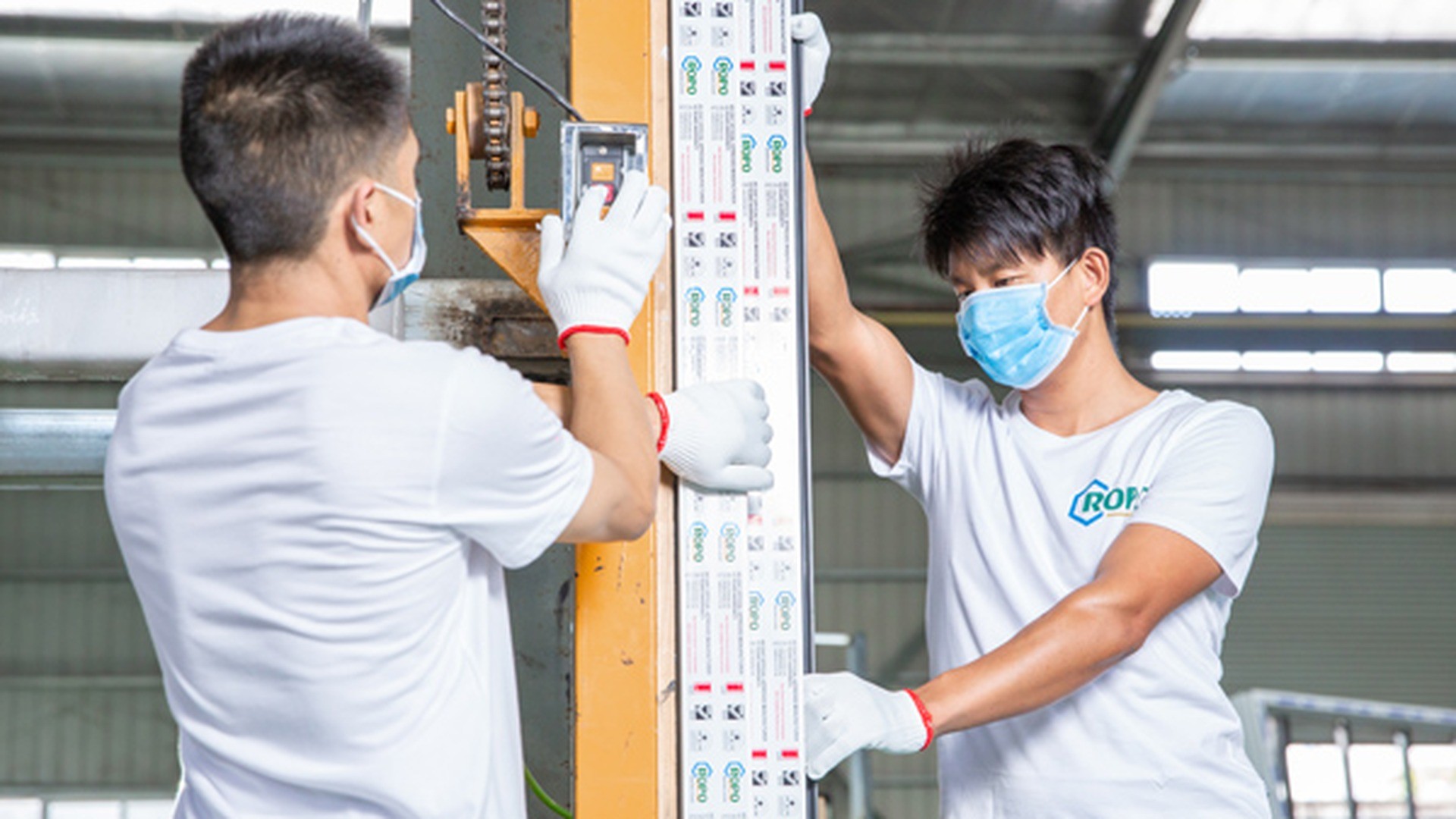 Two operators handling white uPVC profiles on the production floor before assembly.