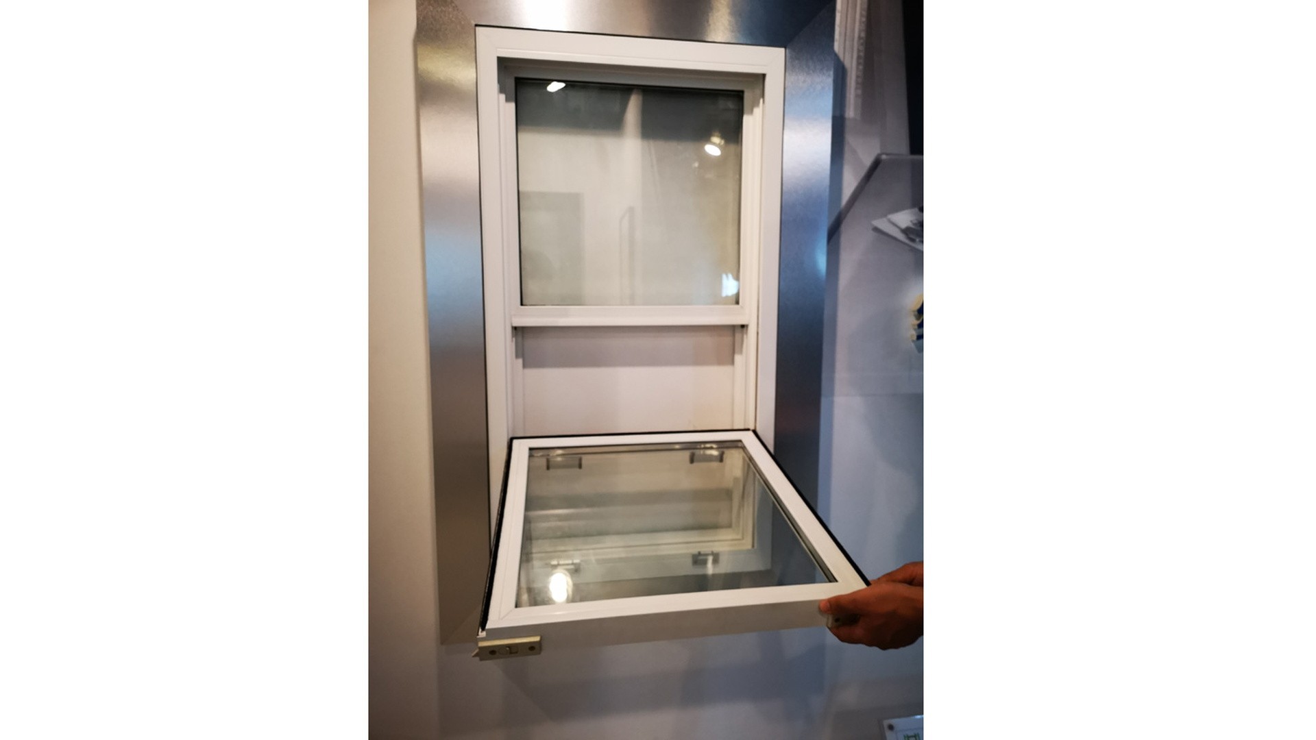 A finished single hung window mounted inside a steel frame, photographed with the lower sash pushed open by hand.