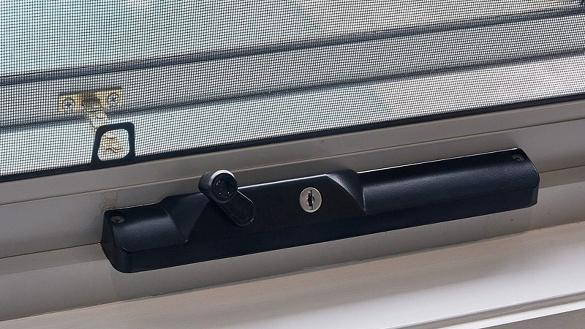 A keyed sash lock on an installed sliding unit, shown with the insect screen and the secondary latch that covers the same opening.
