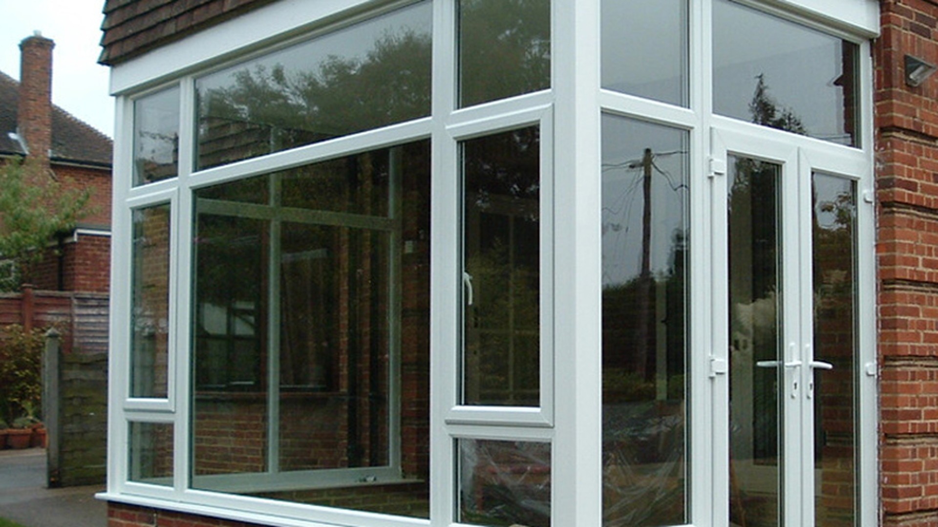 A white uPVC bay window set beside an entrance door on a brick house, the multi-light configuration most residential elevations are built around.