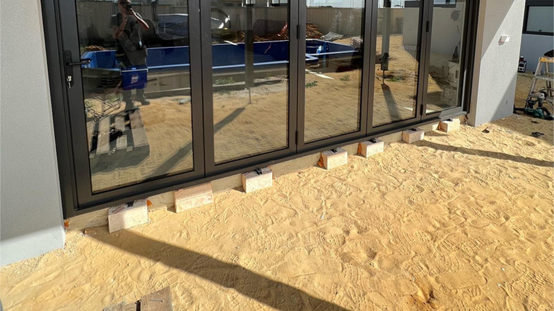 Newly installed aluminium sliding doors photographed at installation stage, with the frame seated on packers along the sill: the fixing detail that decides whether a door stays square and drains correctly.