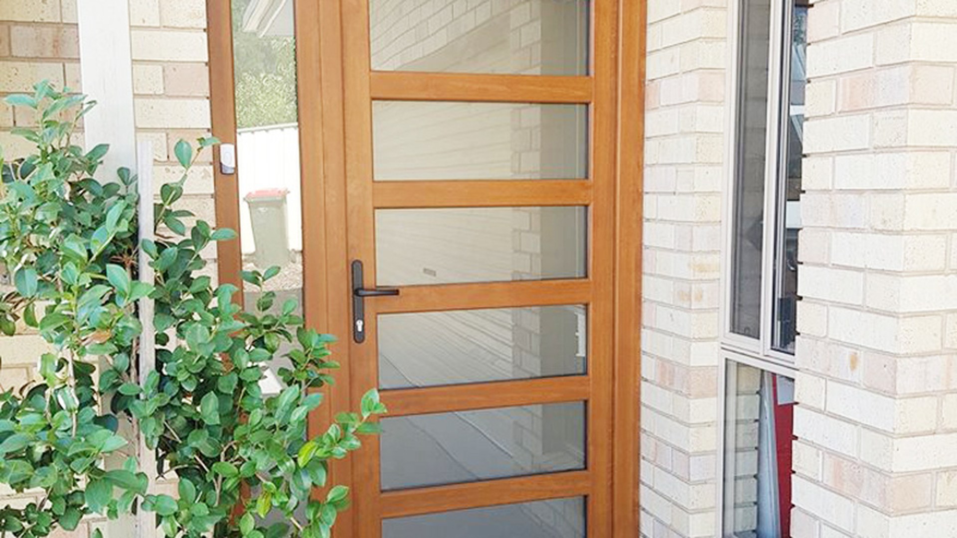 A woodgrain uPVC entrance door with a matching sidelight fitted in a brick facade: the leaf, sidelight and frame arrive as one welded, reinforced and glazed assembly.