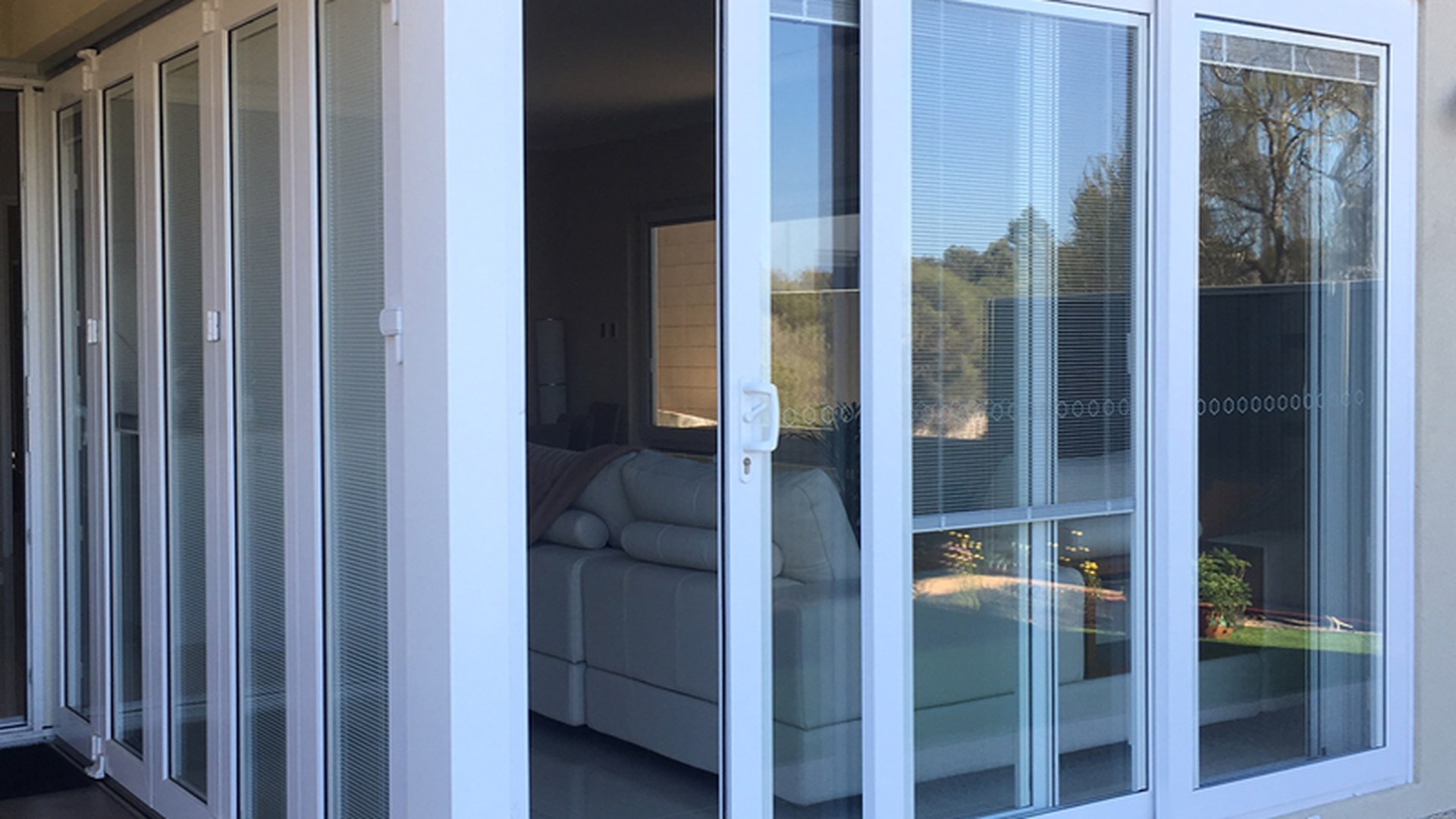 A white uPVC sliding door set with integral blinds, photographed from the frame side: glazing, blinds, hardware and threshold are specified per opening before production.