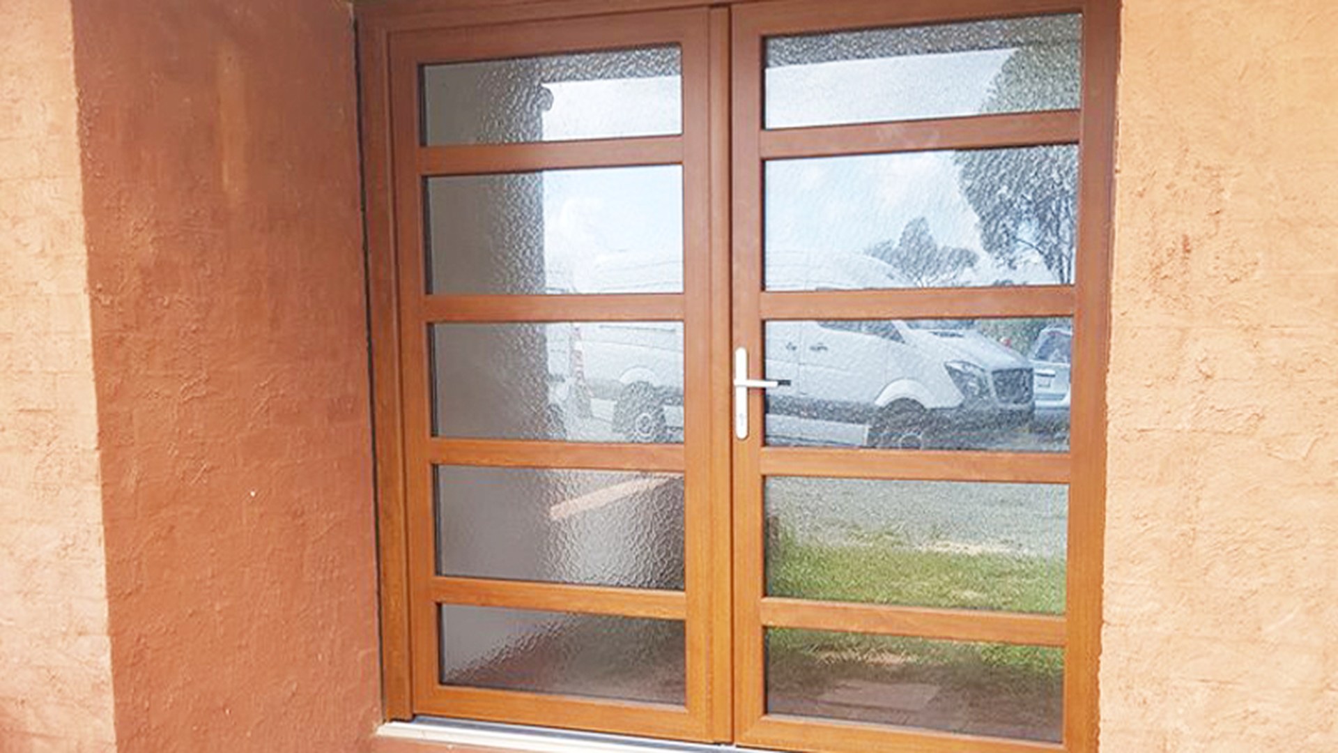 A woodgrain uPVC double door set on a rendered elevation: how the leaves, frame and threshold read once the unit is installed and sealed.