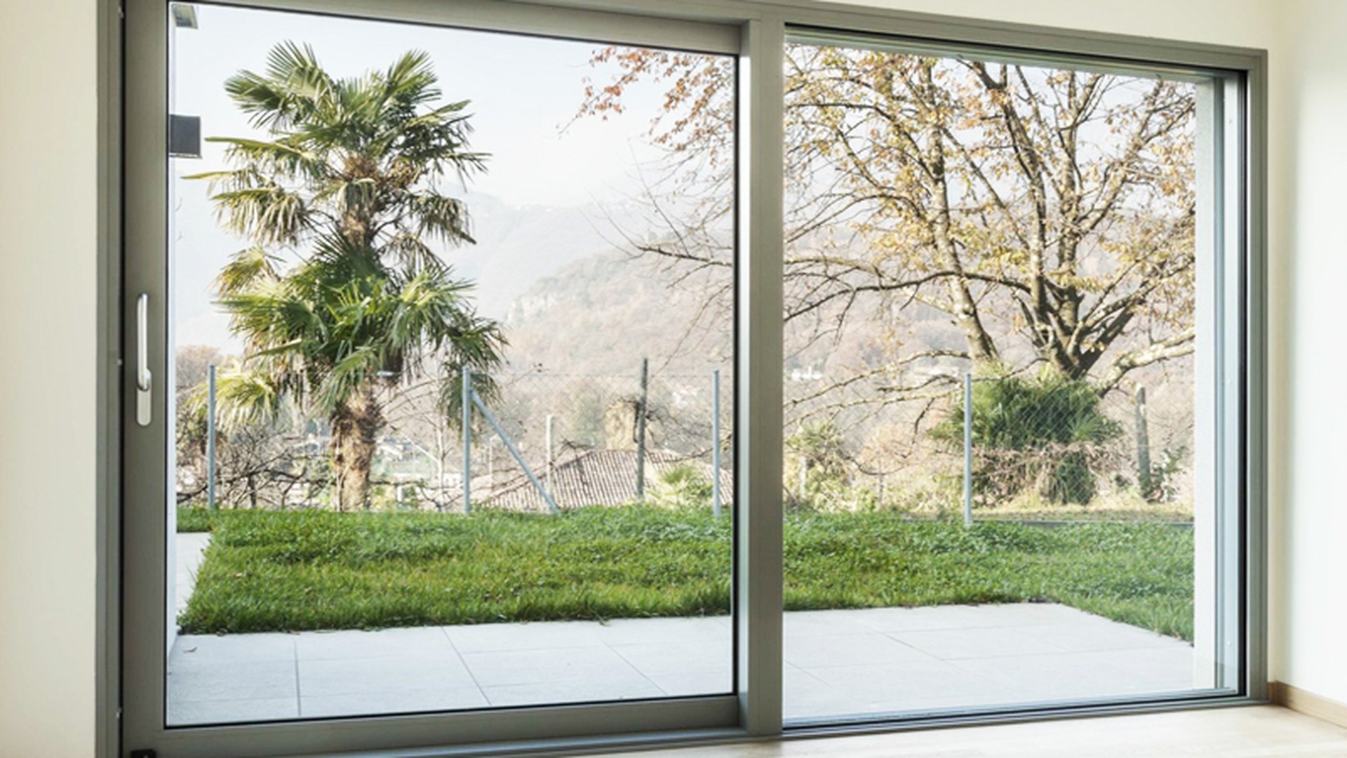 A grey aluminium lift and slide door installed in a finished room, the sash travelling across a full-height opening that looks out onto a garden.