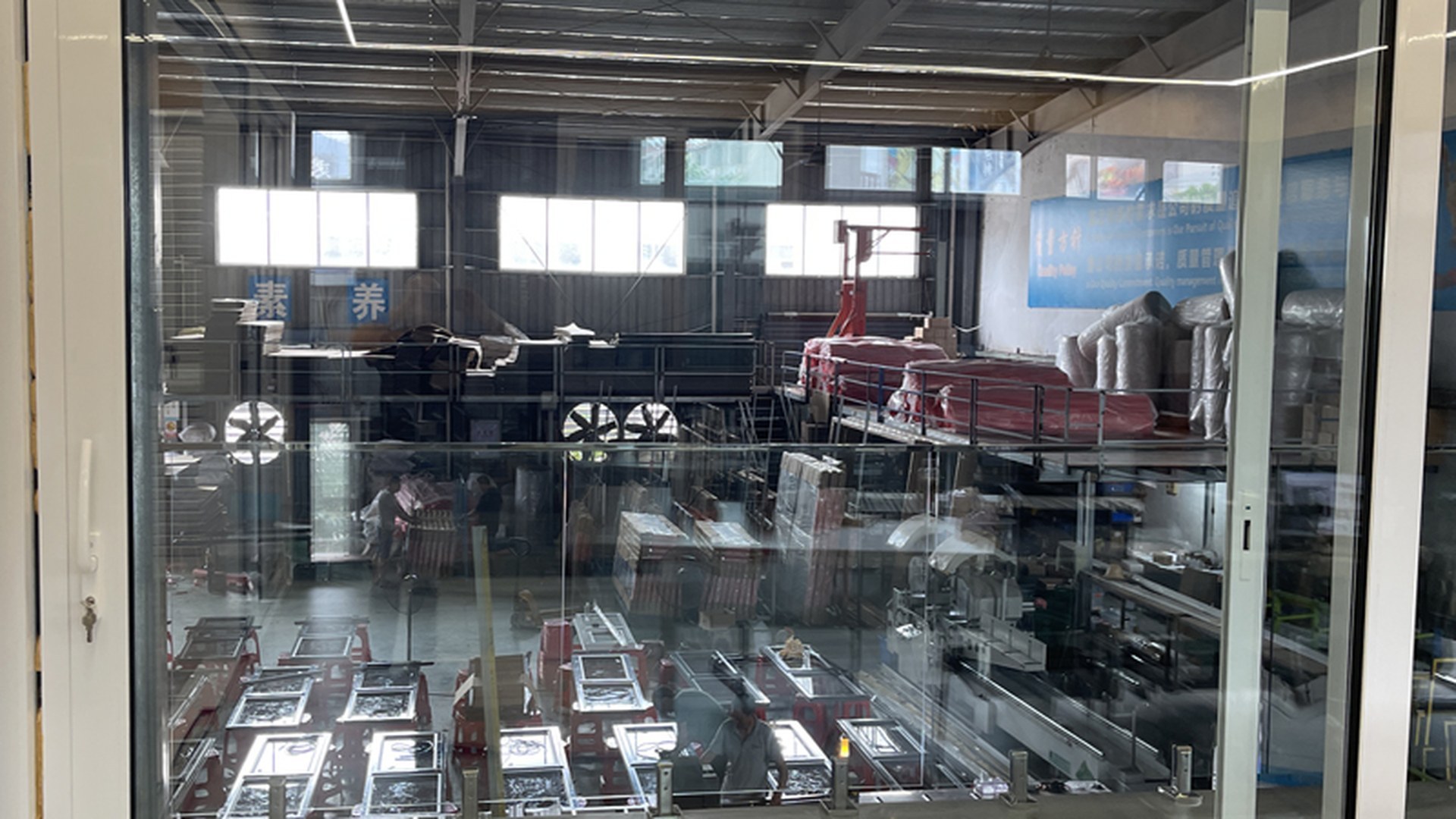 A completed white lift and slide unit standing in the workshop before packing, its frame, glazing and hardware assembled and checked with the production floor visible through the glass.