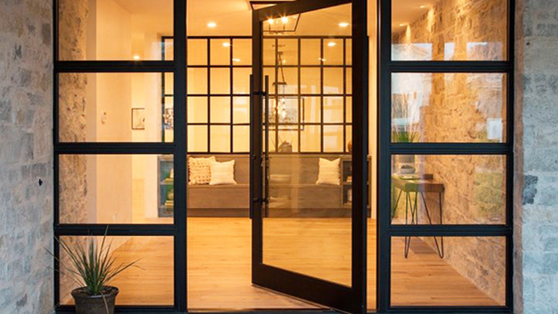 A pivot entrance door with matching glazed sidelights, photographed open in a stone and glass entry: the format specified when the entrance has to read as one continuous plane.