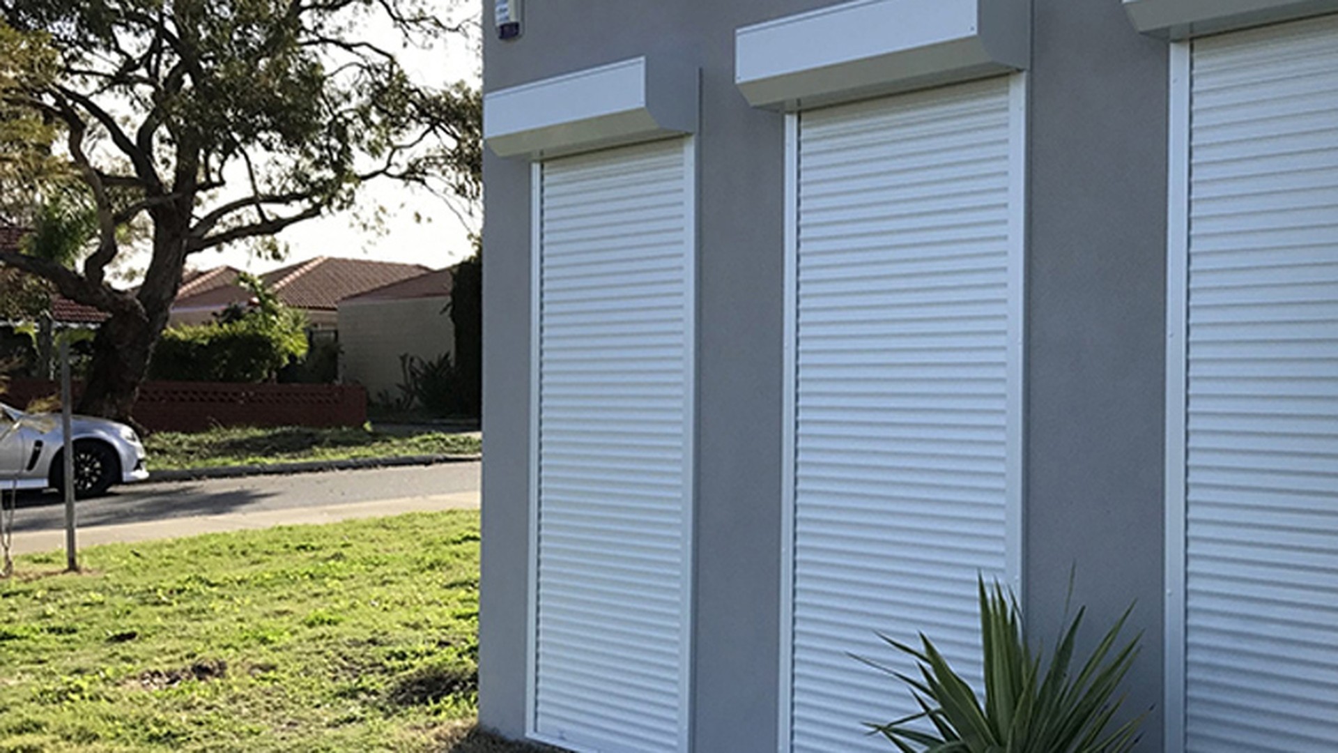 Three white roller shutters closed across a rendered elevation: the head boxes sit proud of the wall, which is the retrofit detail that decides how the guides are fixed.