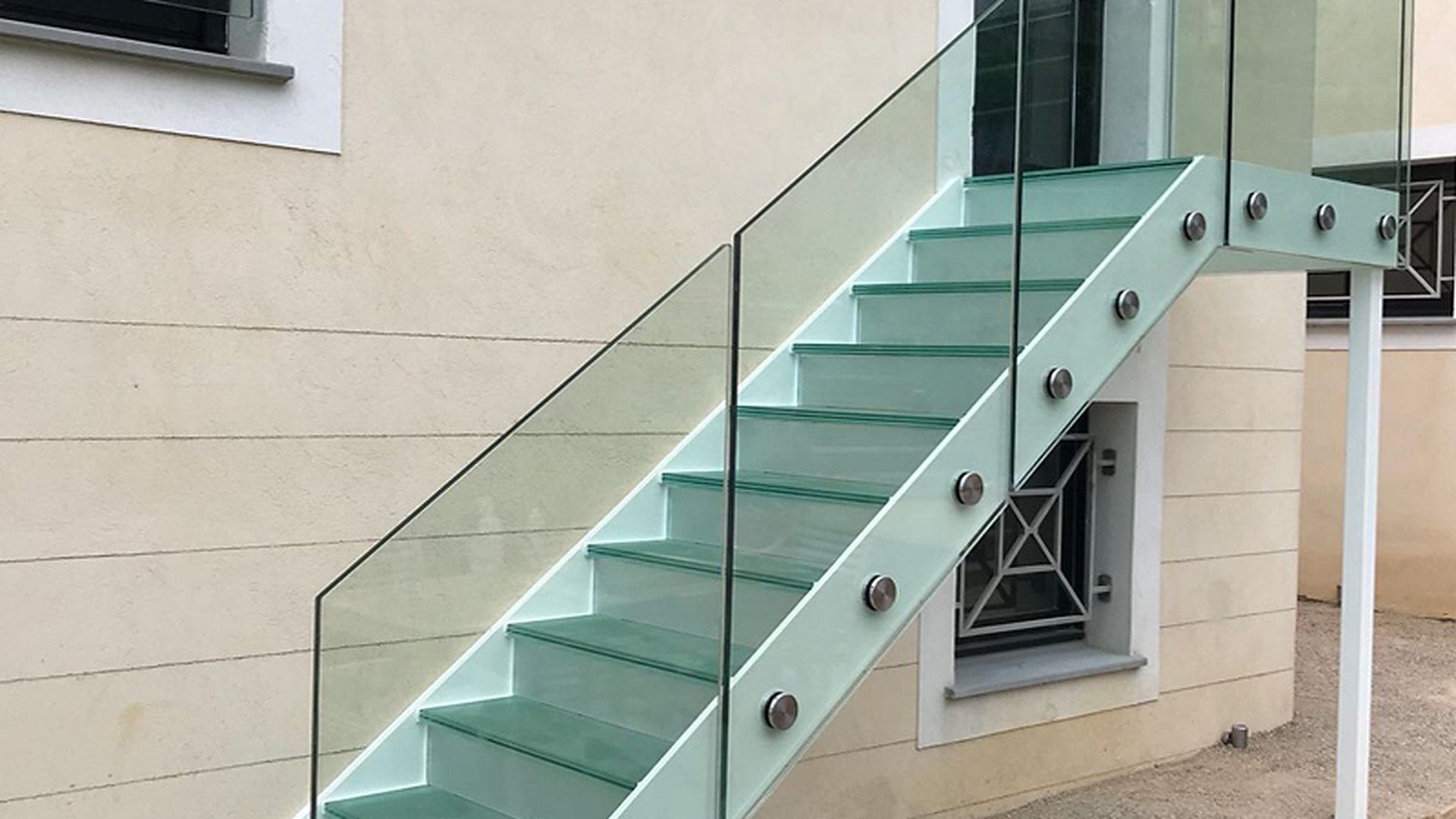 An external staircase with a frameless glass balustrade carried on the outer stringer: the fixings follow the stair pitch, which is where a guard stops being a simple balcony panel.
