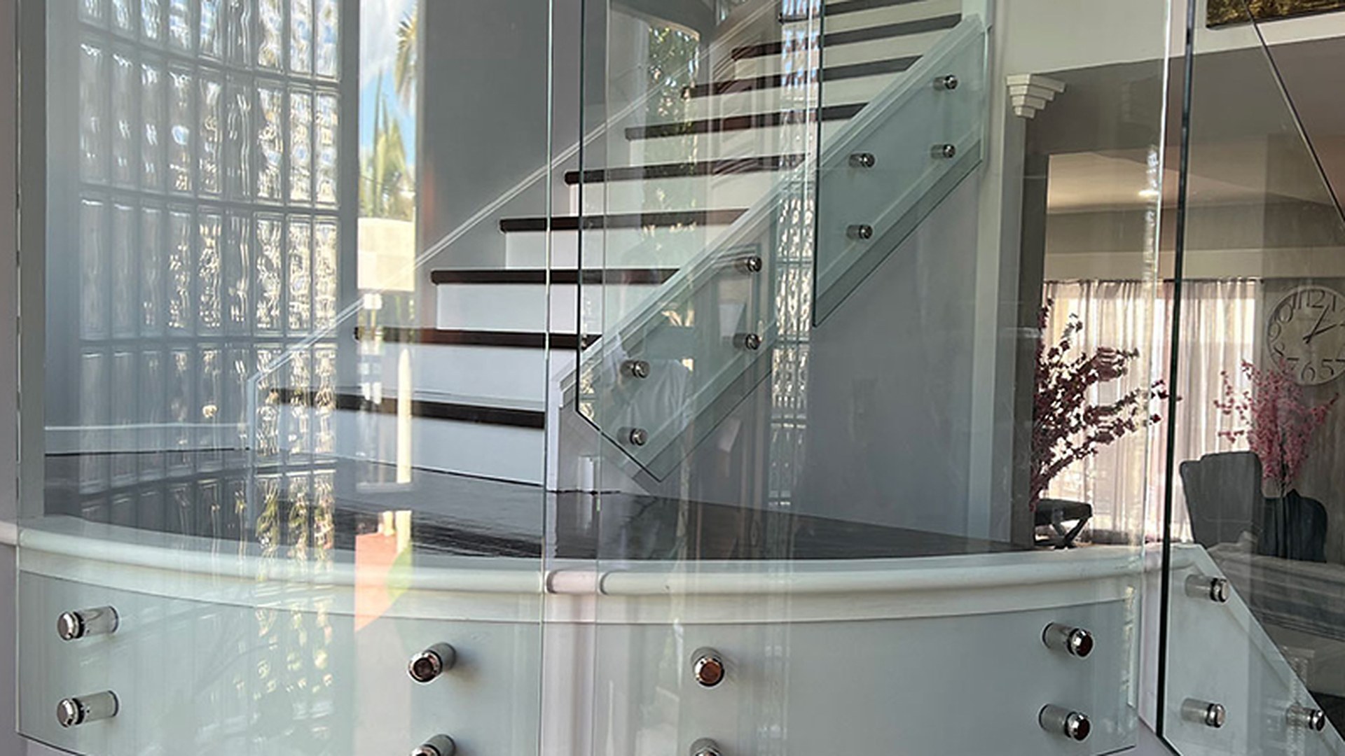 Point-fixed glass on a curved balcony, photographed close enough to read the standoff pattern and the polished top edge: the hole spacing and the edge finish are the two things the calculation depends on.