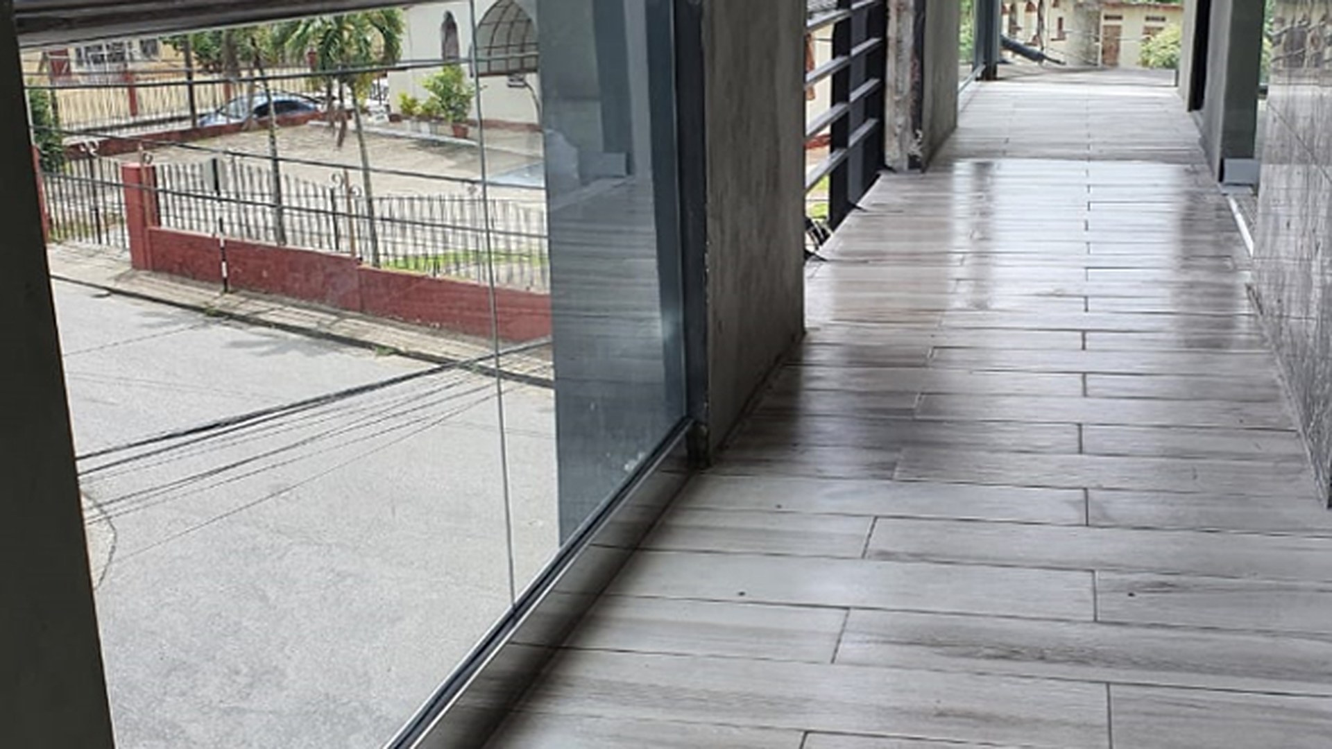 Glass panels set in a base channel along a tiled walkway, with the shoe line and the paving junction both visible: the interface that decides whether the assembly drains or holds water.