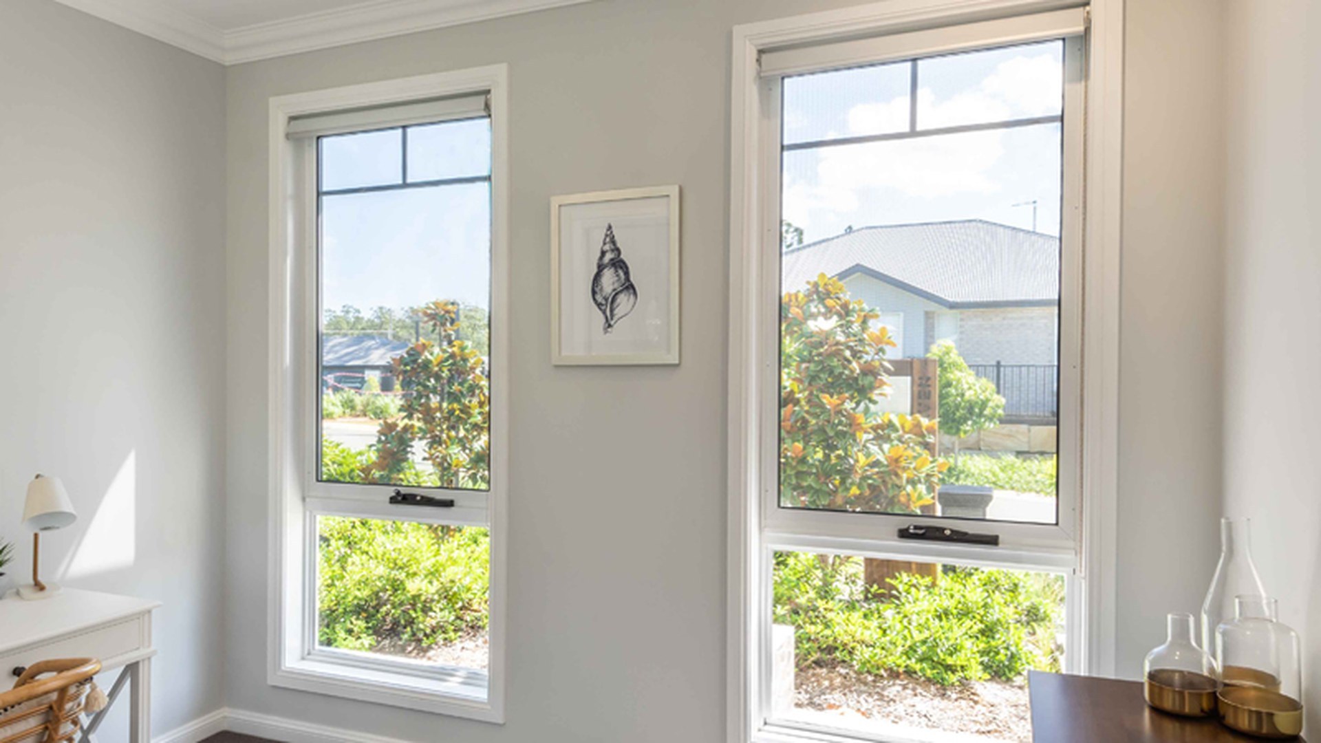 Two white awning windows in a new-build room, both sashes cranked open at the bottom with flyscreens fitted: the airflow path a ventilation-critical room is actually buying.