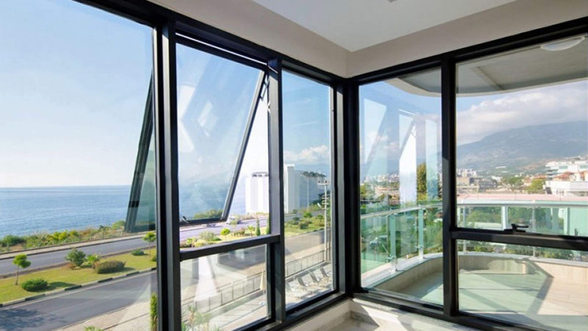 Large black-framed awning windows left open in a coastal apartment: the sash acts as its own rain hood, which is why this window type stays usable in weather that closes a casement.