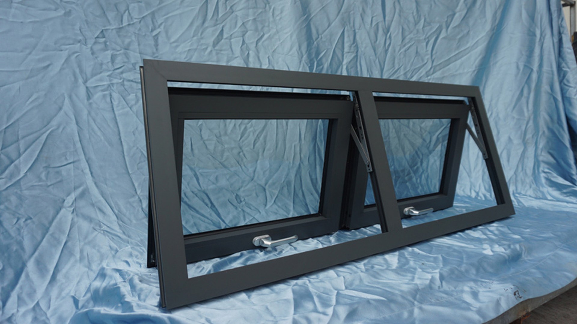 Two awning sashes on a dark frame with the friction stays visible at the jambs, showing how far the sash projects and where the hinge line sits in the outer frame.