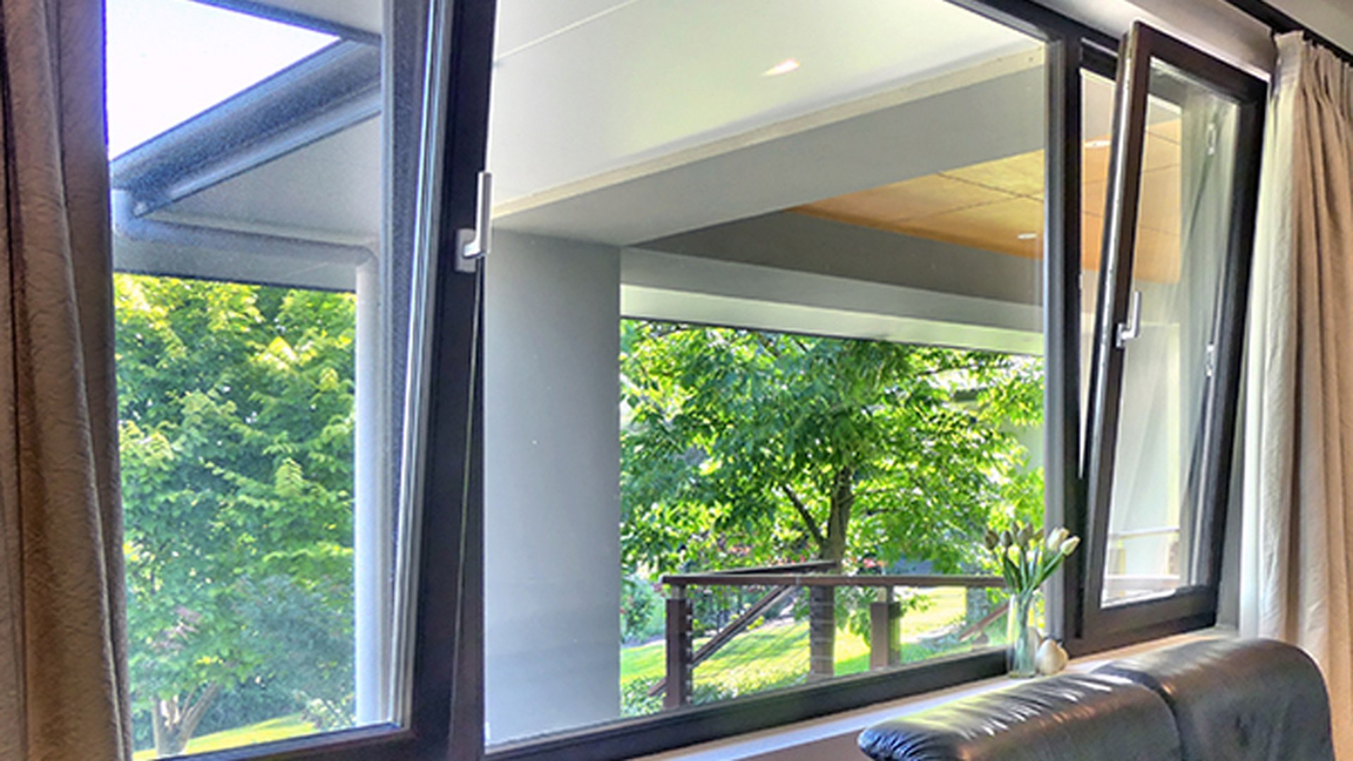Two sashes turned fully inward onto a garden in a dark-framed opening: the "turn" half of a tilt and turn window, with the handles clear of the fixed pane beside them.