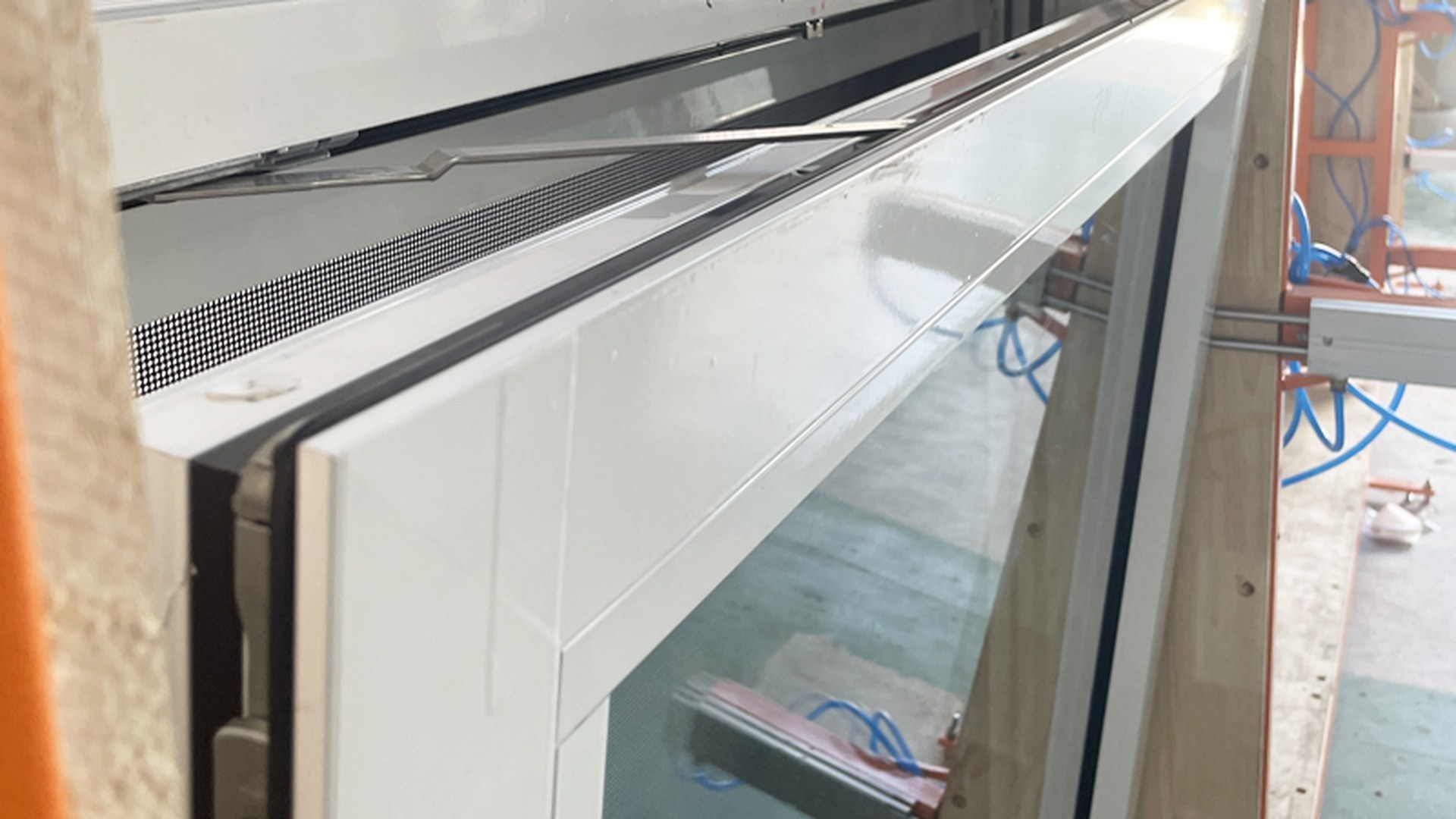 A tilt sash held at the assembly bench with the flyscreen already in its rebate: the gap at the bottom of the sash is the whole ventilation opening, and the screen is what decides how much of it survives.