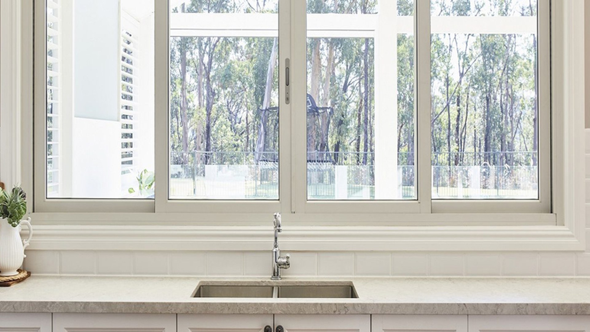 Three sliding sashes above a sink run, with the fixed pane at the end: the whole elevation is glass, and the only moving parts are the two sashes and their track.