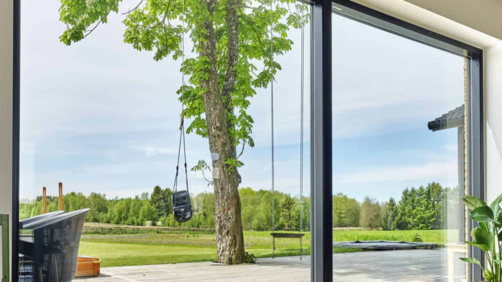 A wall of glass with no handles and no sashes: slim black fixed frames run from floor to ceiling, and the only opening in the room is somewhere else entirely.