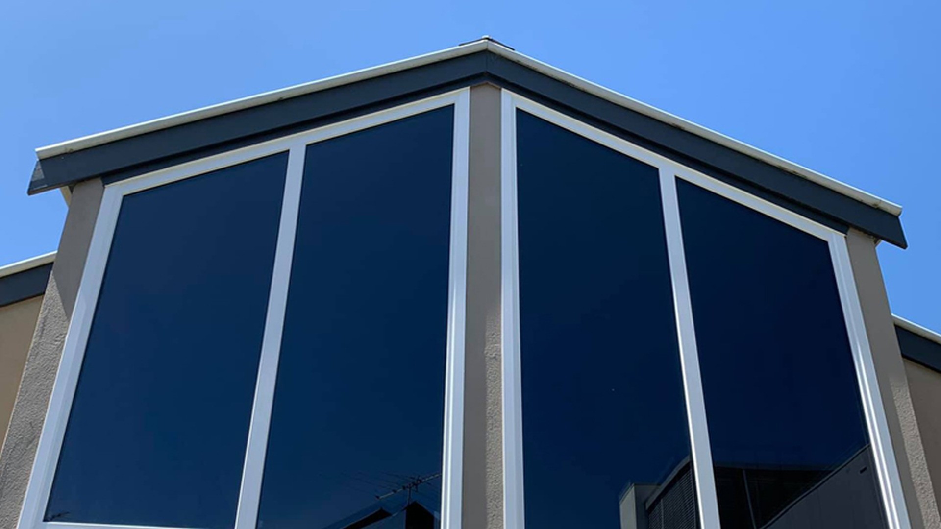 Fixed lights on an upper storey, seen from outside: two faces of glass meet at a corner post, and every pane is dead glass held only by its frame and the wall opening.