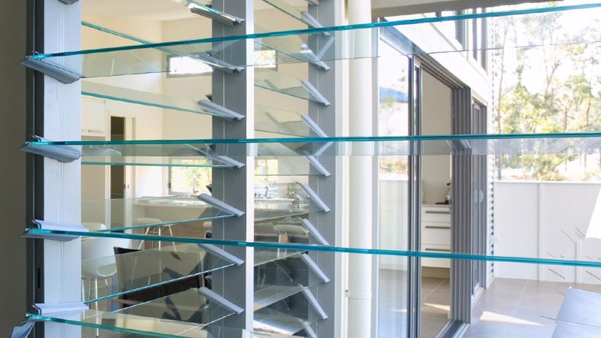 Glass blades held in a row of aluminium shoes: the blade carrier, not the frame, is what sets the spacing and the angle on a frameless louver screen.
