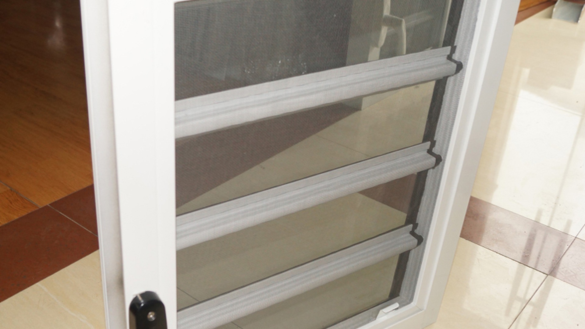 Frame, flyscreen and blade stack in one unit: the screen sits on the inside face, and each blade closes against an EPDM seal rather than against glass.
