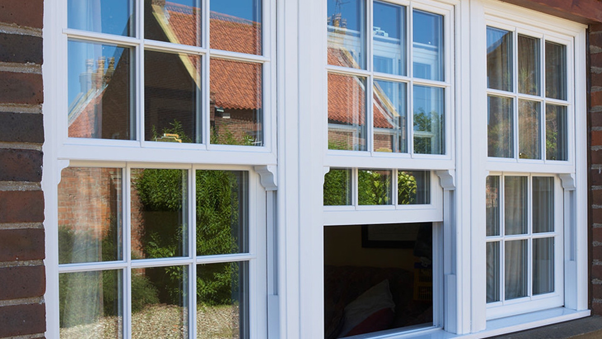 A traditional brick elevation in white uPVC: the centre light has its lower sash raised, so the check rail, the sash stiles and the depth of the frame are visible at once.
