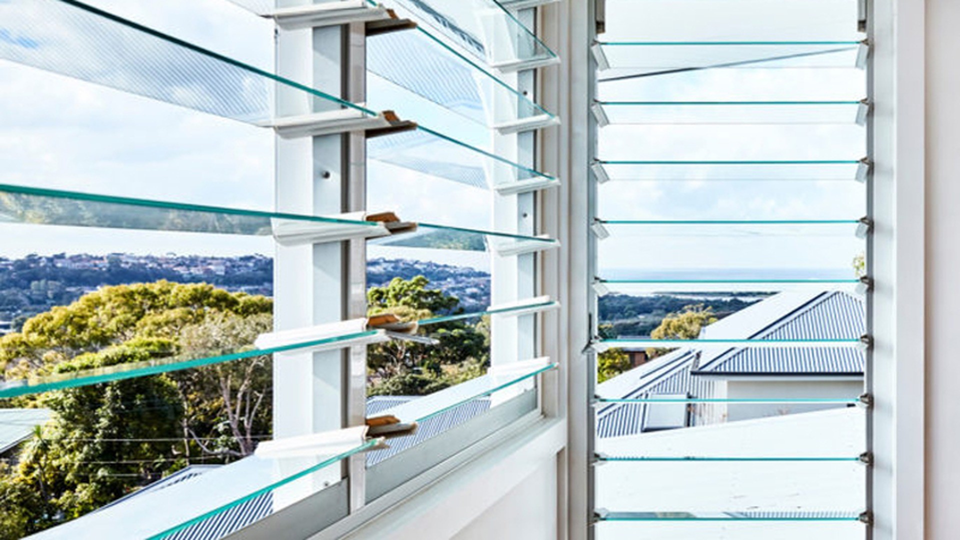 An installed bank on an exposed elevation: the blades can stay part open in light rain, and the flyscreen behind them is specified with the unit rather than added on site.