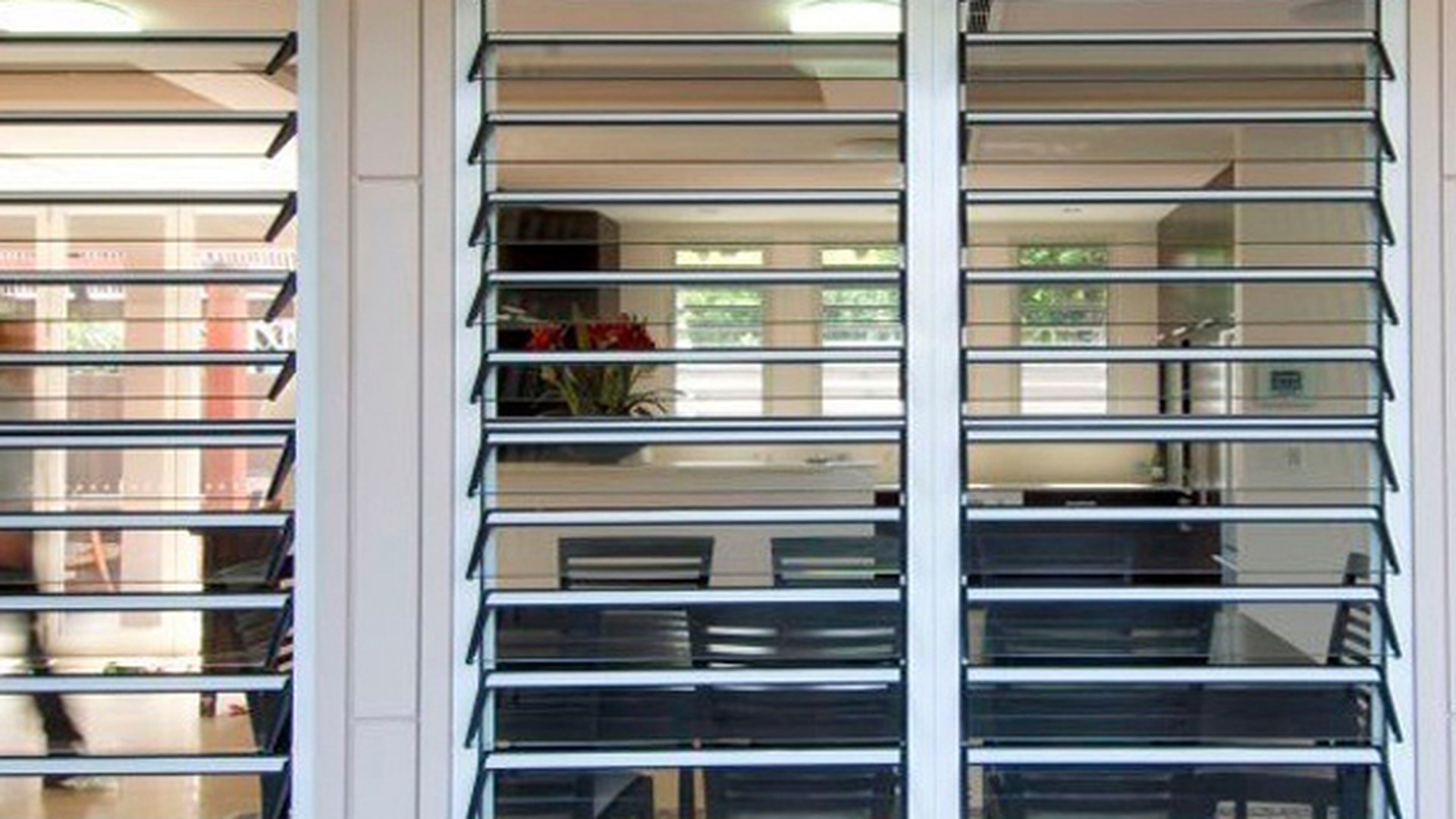 Two glass louver panels set side by side in a wall opening, blades tilted open: in a tropical room the window itself is the ventilator, and the view behind it stays uninterrupted.