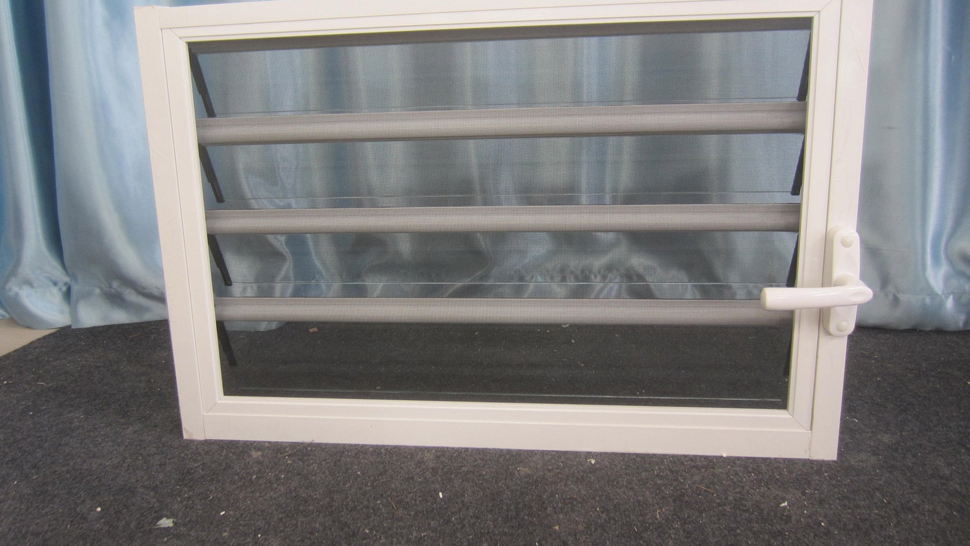 A complete louver unit on the bench before packing: blades, face-mounted flyscreen, operating handle and frame gasket, with nothing hidden behind a sash because there is no sash.