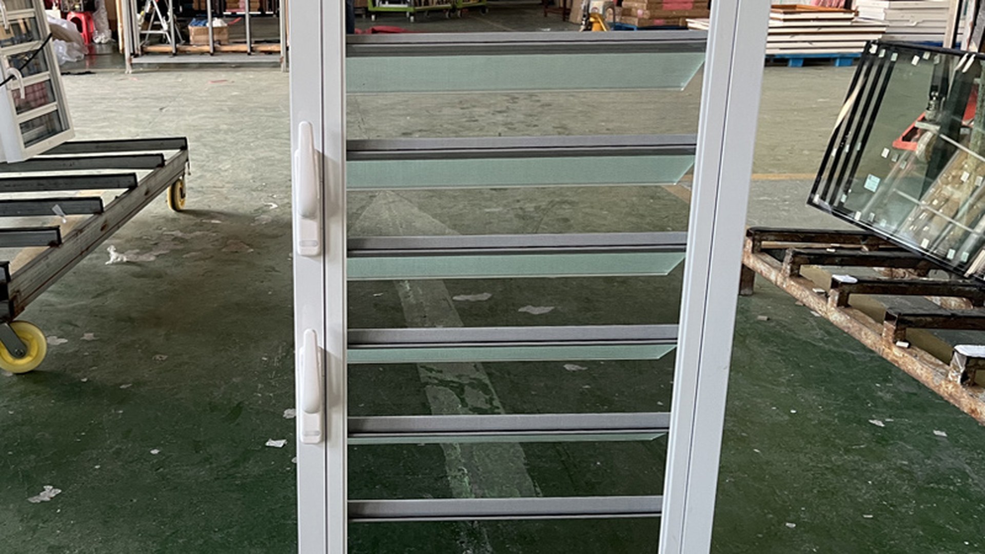 A full-height louver gallery standing on the factory floor with the blades open: the frame, blades and linkage are assembled and glazed as one unit, then crated upright.