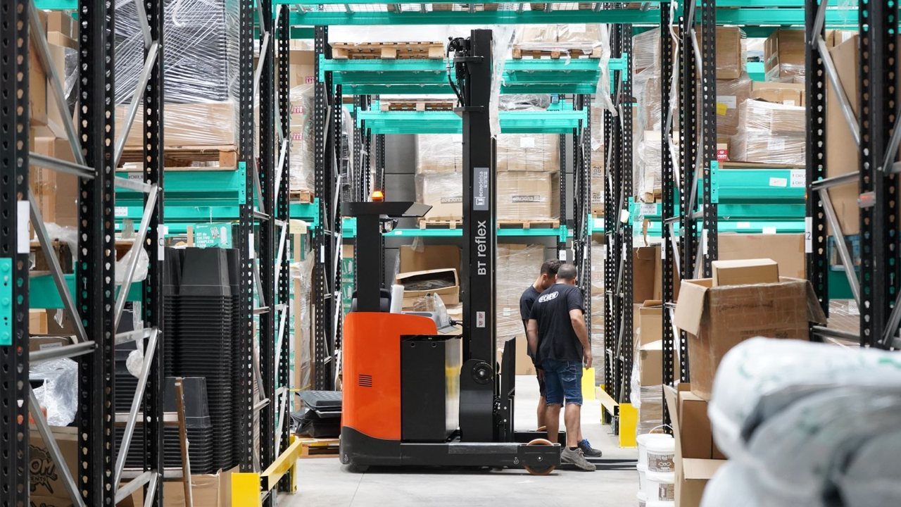 Warehouse workers with a reach truck moving palletised stock between racking aisles
