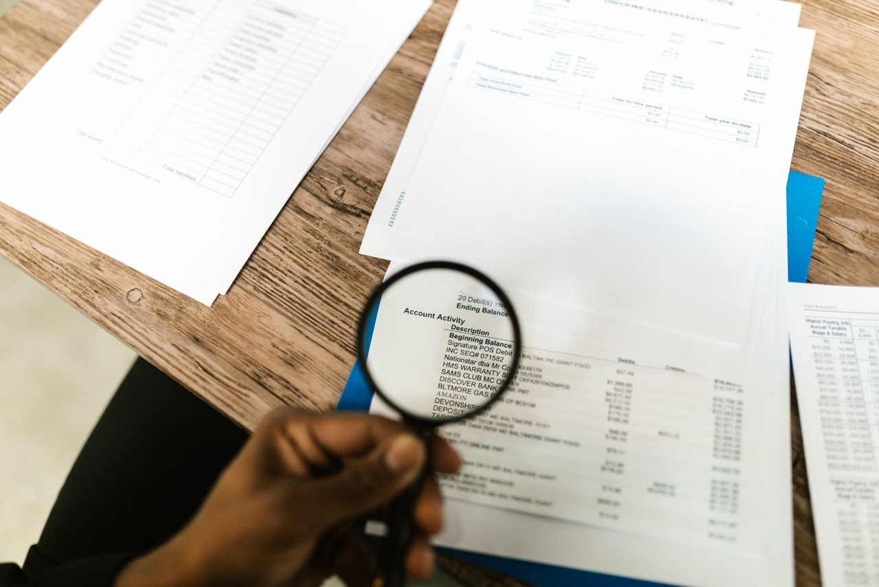 Close-up of a hand using a magnifying glass to examine figures on an invoice