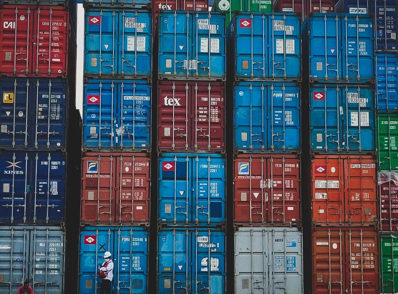 Stacked intermodal shipping containers at a seaport with a worker in a hard hat.