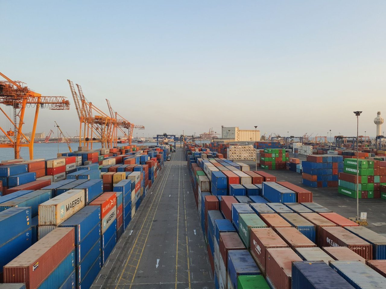 Stacked shipping containers and gantry cranes at a seaport, representing the freight, duty and clearance costs behind landed cost per unit.