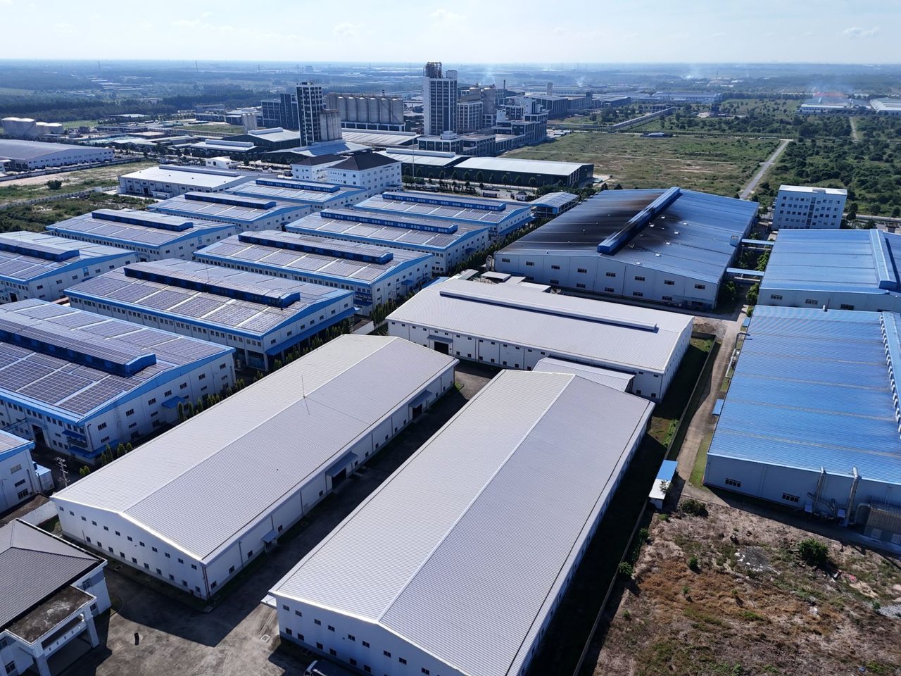 Aerial view of an industrial park with rows of large factory roofs and rooftop solar arrays, the footprint pattern a satellite or street-view check verifies.