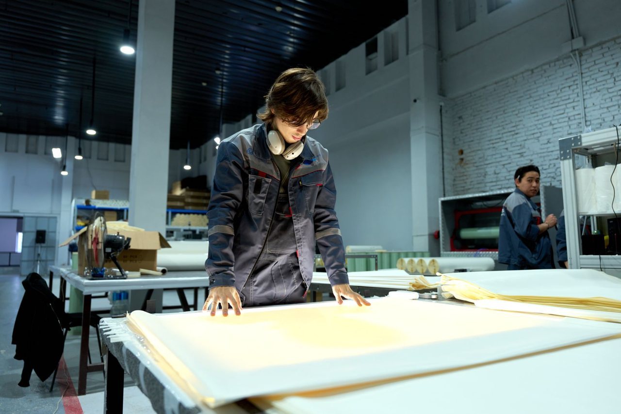 An inspector examining a large material sheet at a workbench inside a factory during an unannounced walkthrough.