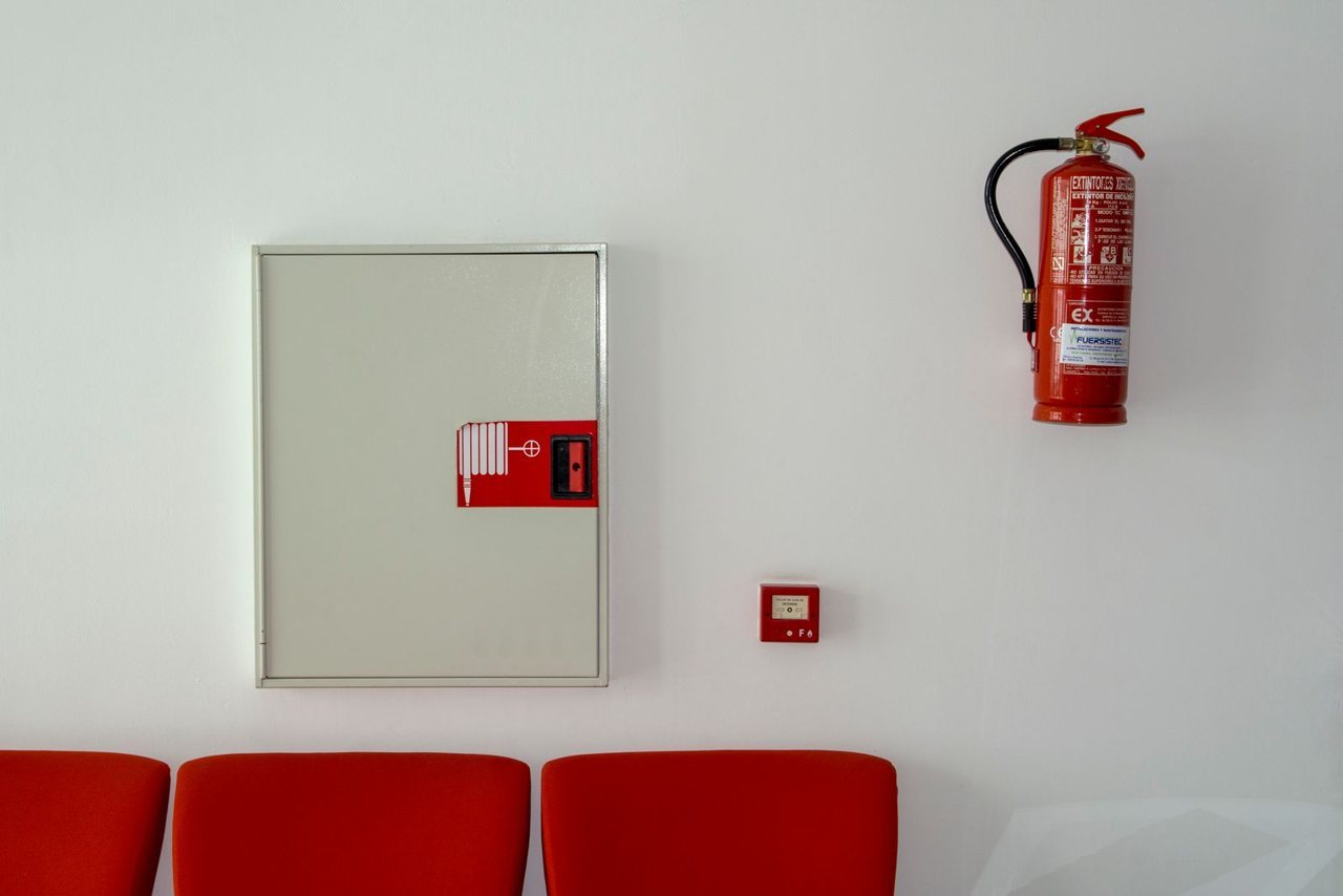 A wall-mounted fire extinguisher and fire-hose cabinet in an office corridor, the monthly-inspected fire equipment a social-compliance auditor checks first during the site walk
