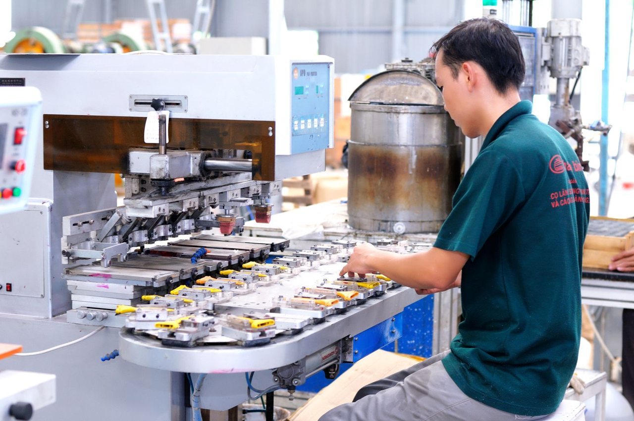 A factory operator in uniform and gloves working at production machinery mid-run, the stage where a during-production inspection can still catch drift cheaply