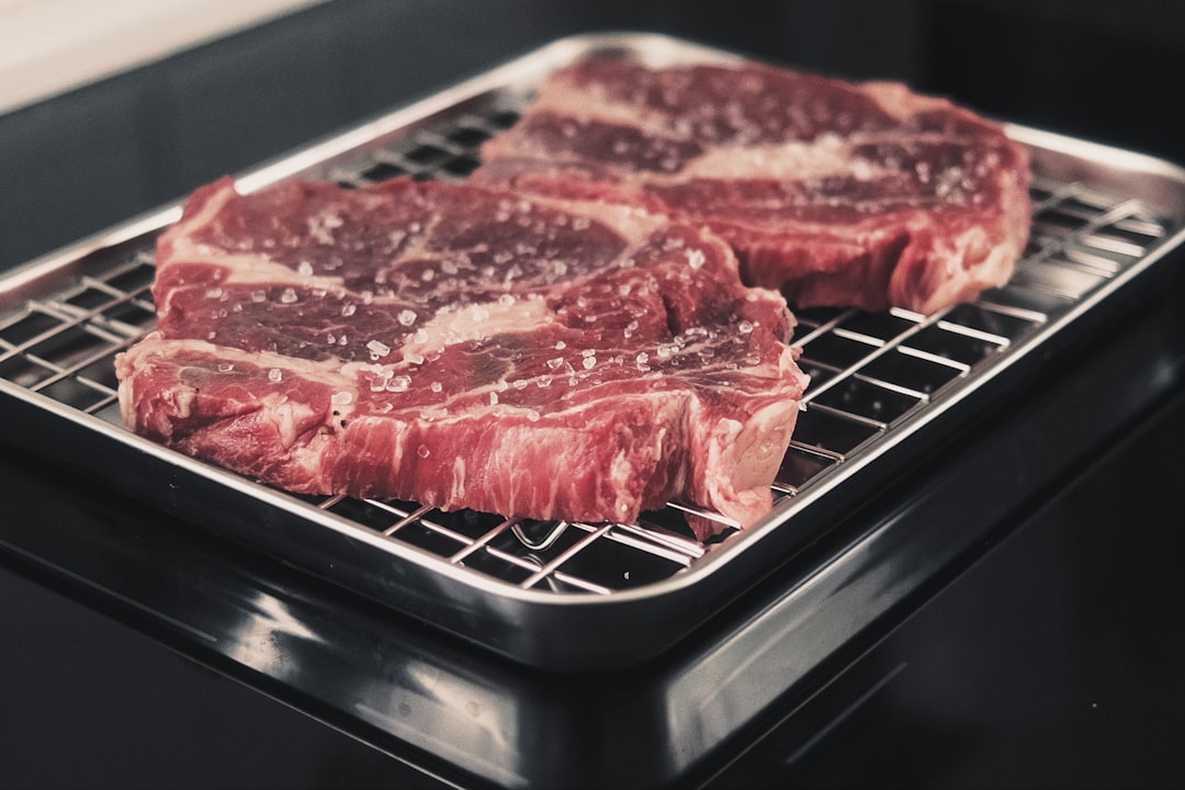 A large, beautifully marbled cut of beef aging on a rack inside a sleek, stainless steel dry aging fridge with a glass door.