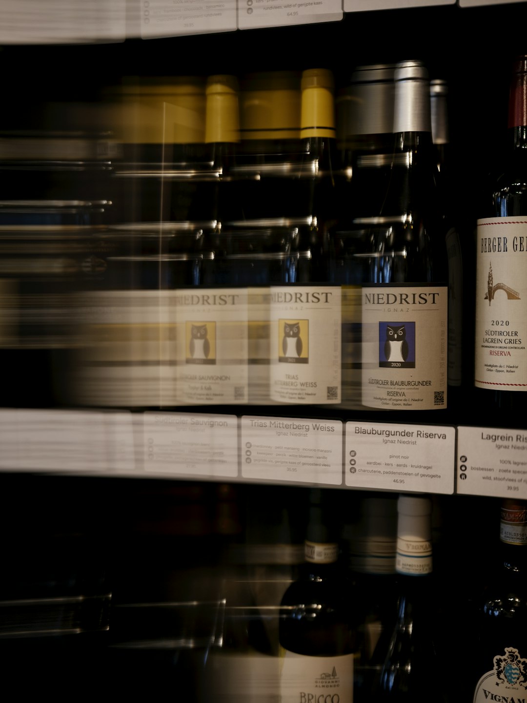 A close-up of wine bottles on adjustable wooden shelves inside a wine cooler with blue LED lighting