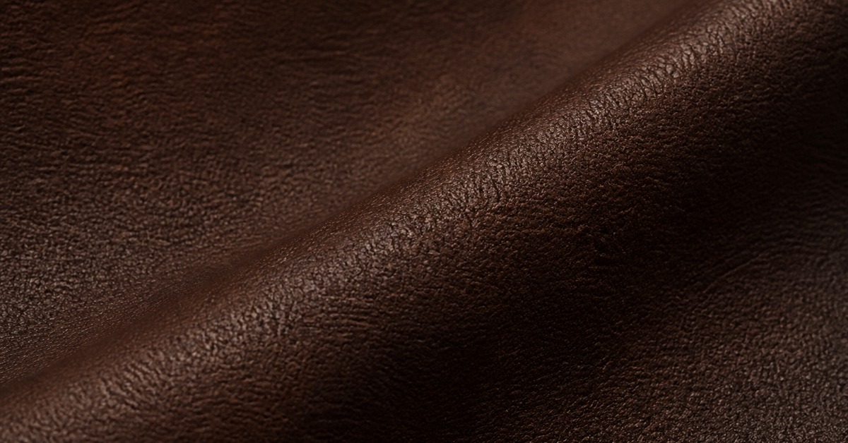 Close-up of a dark brown full-grain leather surface showing pore texture and a soft fold for leather jacket production