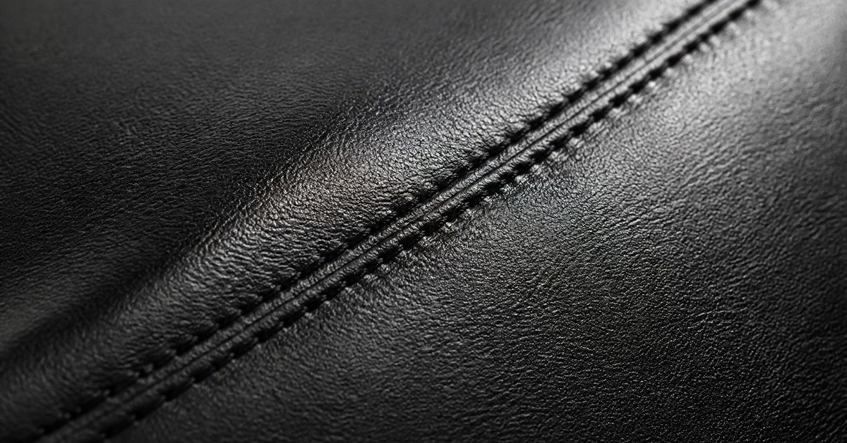 Close-up of black full-grain leather showing natural pore texture and a double-stitched seam for a leather jacket article