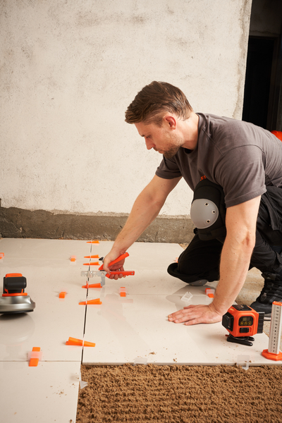 Professional tiler driving wedge into clip with pliers during tile installation