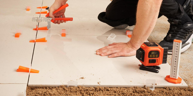 Tiler using tile leveling system with pliers, clips and laser level on white tile floor