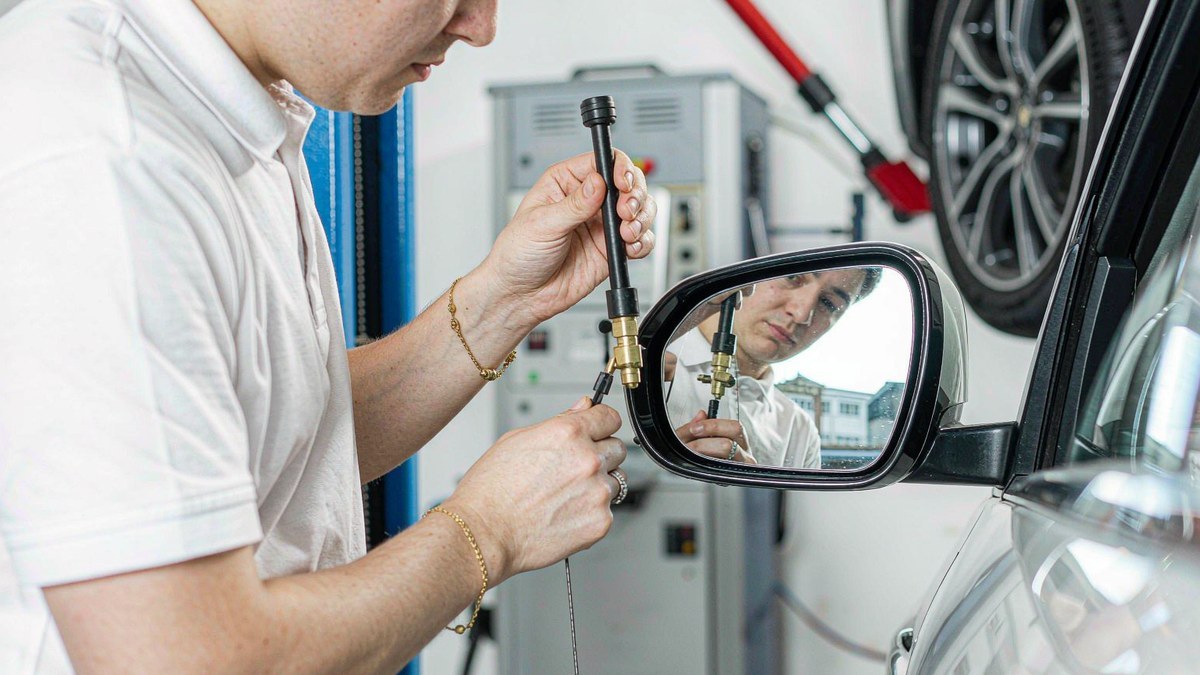 Technician adjusting a car side mirror in a workshop