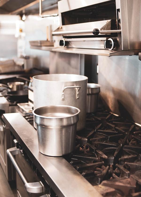 Stainless steel stock pots cooking on a commercial gas stove in a hotel catering kitchen