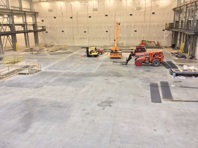Factory workers preparing a clean concrete foundation for a decoiler machine installation
