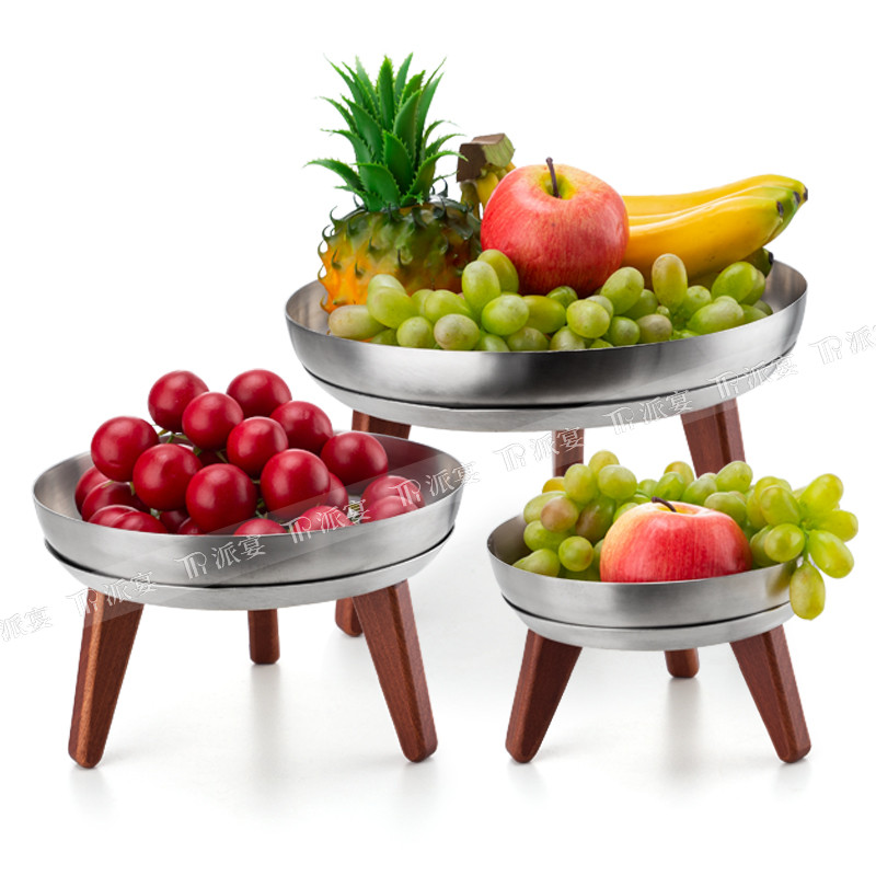Serving bowls with fruit placed on low buffet display stands with wooden legs