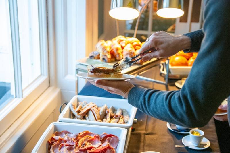 person serving breakfast buffet with bacon and pastries at hotel