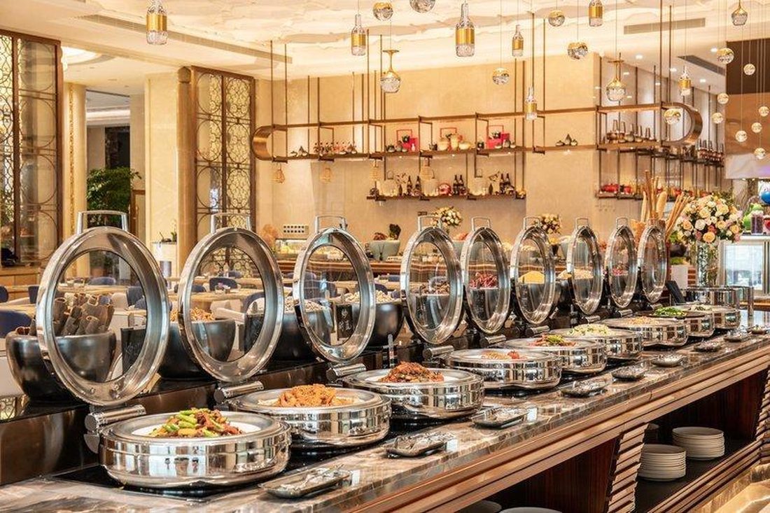 Chafing pan sizes shown on glass-lid round chafing dishes holding hot food on a hotel buffet counter